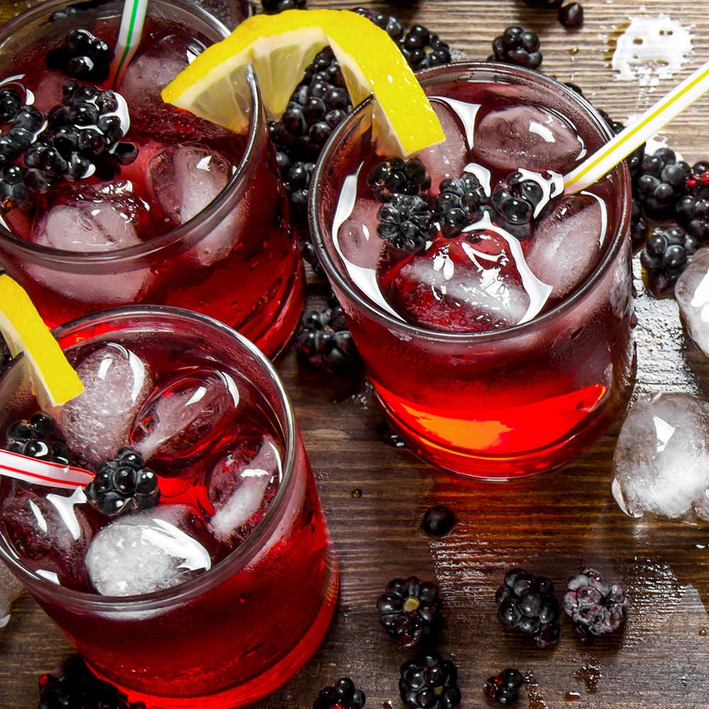 Glasses of ice cold blackberry lemonade with fresh blackberries and lemon wedges, indicating flavor of "F*ck The Lemons" lip balm by EXOH.