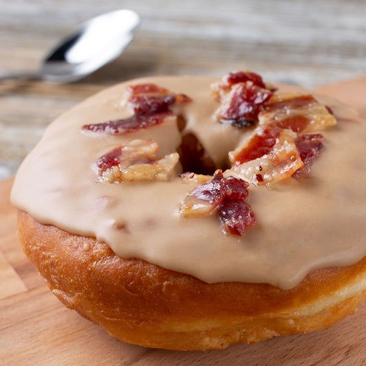 Maple-glazed round doughnut topped with crumbled bacon, indicating scent of "Forbidden Dooonut" flavored lip balm by EXOH.