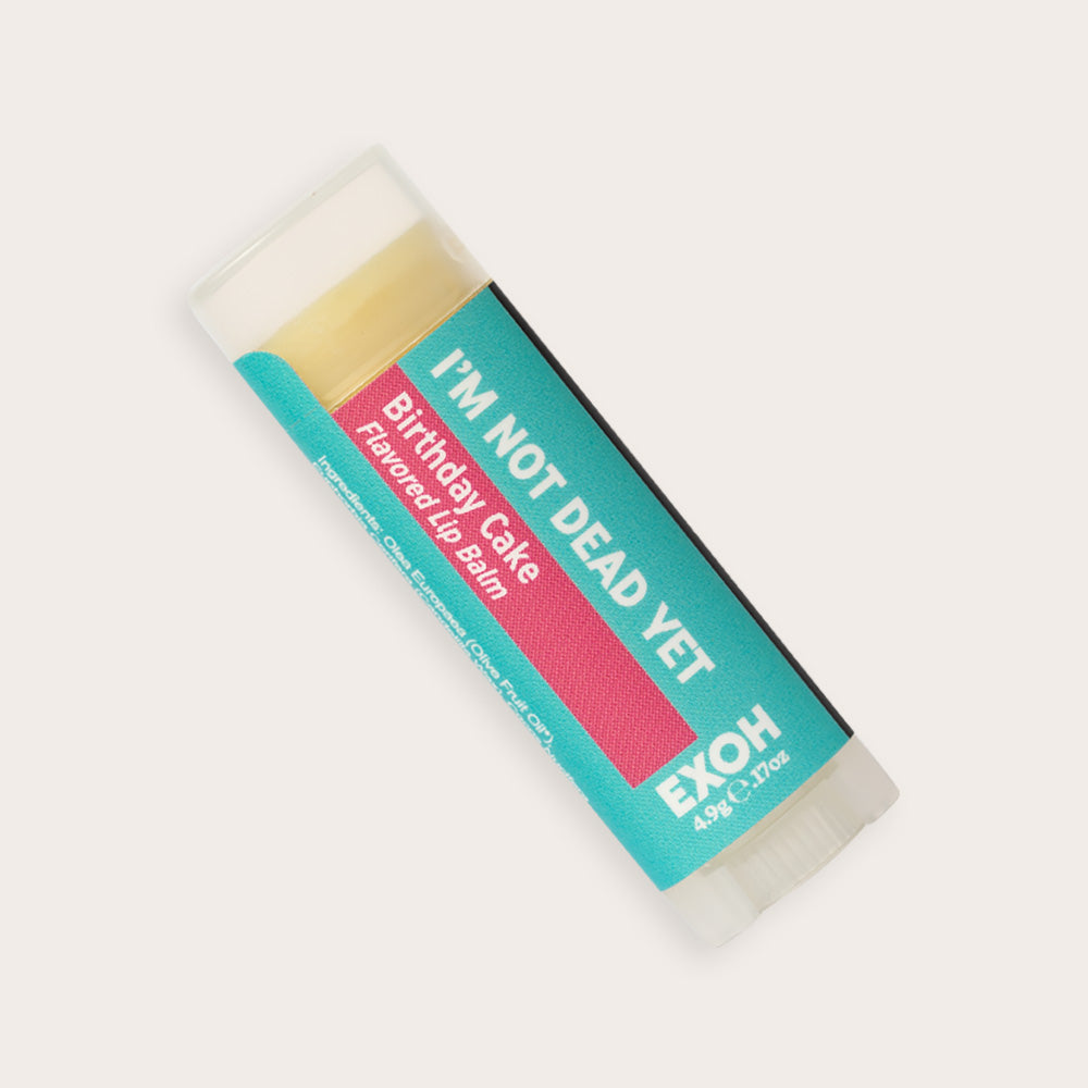 Product photo of birthday cake flavored lip balm "I'm Not Dead Yet" by EXOH on grey background.